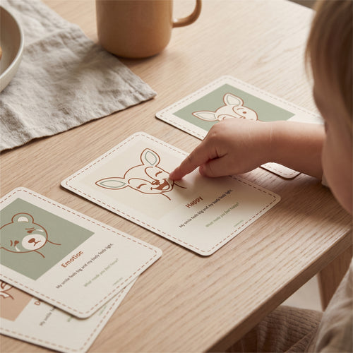 A young child pointing at a printed Fawnling feeling card on a kitchen table